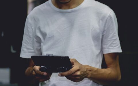 A young man in a white shirt using a smartphone game controller indoors.