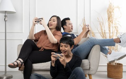 Three friends enthusiastically playing video games indoors, having fun and relaxing.