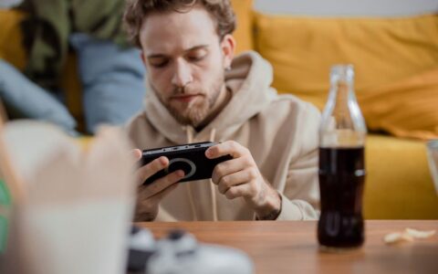 Young man focused on mobile gaming while relaxing indoors with a soft drink.