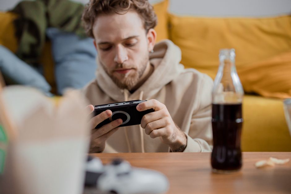 Young man focused on mobile gaming while relaxing indoors with a soft drink.