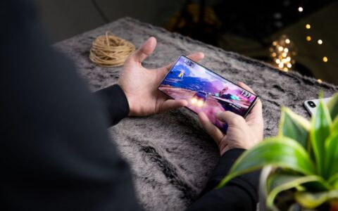From above of crop anonymous person playing video game on modern cellphone with image of car on screen