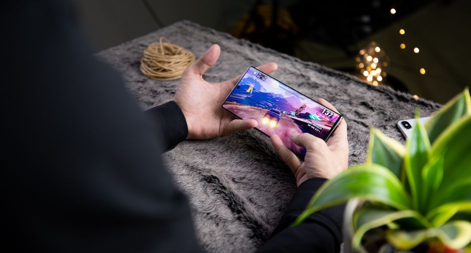 From above of crop anonymous person playing video game on modern cellphone with image of car on screen
