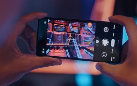Close-up of hands holding a smartphone, photographing an arcade game screen.