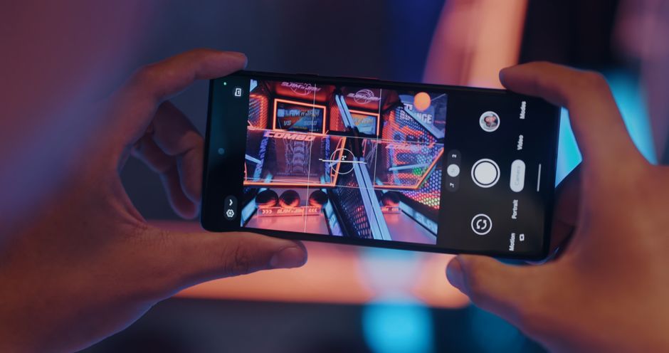 Close-up of hands holding a smartphone, photographing an arcade game screen.