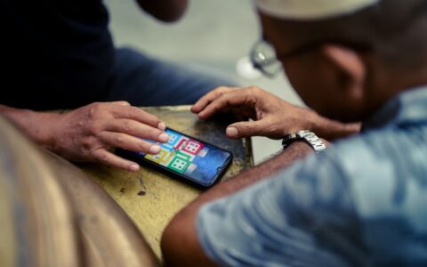 Two individuals play a mobile game on a smartphone outdoors in Jakarta, Indonesia.