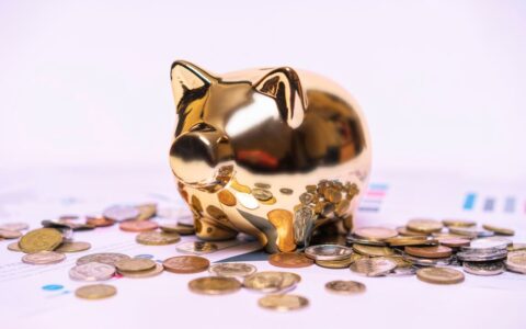 Shiny golden piggy bank on financial documents with scattered coins symbolizes savings.