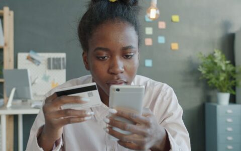 Focused woman using smartphone and credit card in modern office setting for online shopping.