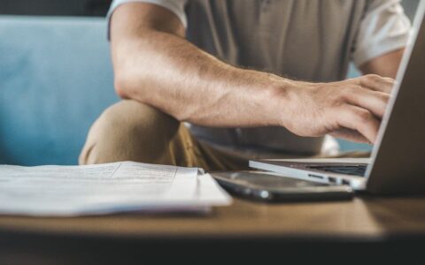 A man typing on a laptop at home, using wireless technology.