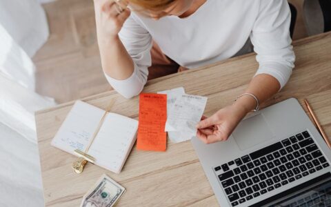 Woman reviewing receipts and planning budget using a laptop and notebook at home to manage expenses.