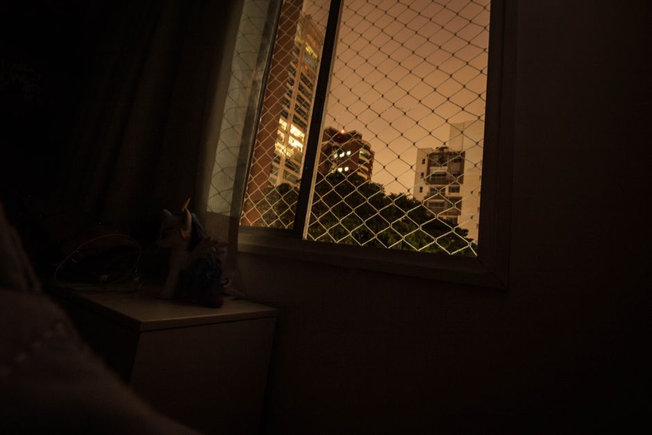 A night view of city buildings from inside a room with a mesh-covered window.