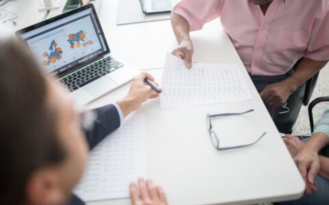 Senior couple reviewing documents with consultant at office desk with laptop.