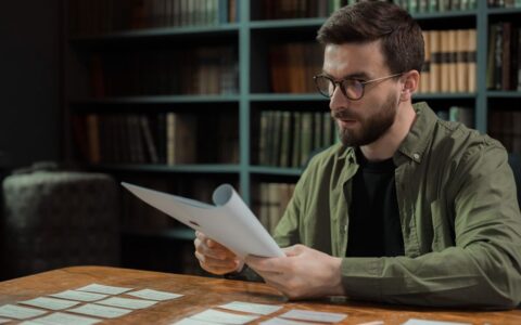 A focused man with glasses carefully reviews documents at a library desk.