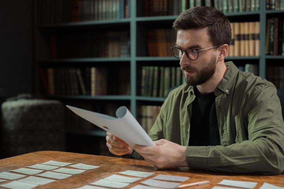 A focused man with glasses carefully reviews documents at a library desk.
