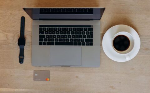 Flat lay of a laptop, smartwatch, credit card, and coffee on a wooden table. Perfect for tech-savvy professionals.