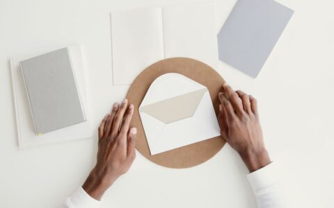 Overhead shot of hands arranging an envelope among notebooks on a minimal workspace.