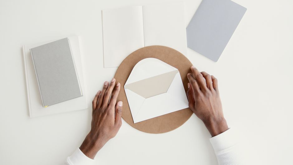 Overhead shot of hands arranging an envelope among notebooks on a minimal workspace.