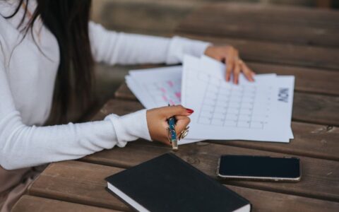Side view of crop unrecognizable ethnic female office employee working with papers representing month plan