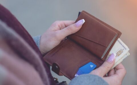 Close-up image of hands holding a brown leather wallet with banknotes and a credit card visible.