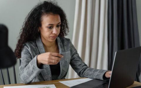 Professional woman at desk with credit card, laptop, and cash. Expression of concentration.