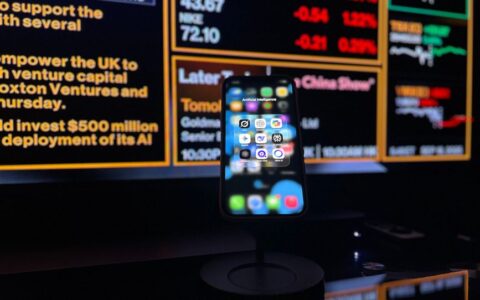Smartphone displaying AI apps in front of a financial data screen in London.
